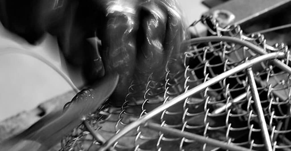 Main floue en mouvement tenant un outil, travaillant sur une grille métallique.